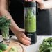 A person making a healthy green smoothie with fresh vegetables in a modern kitchen.