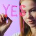 Teenage girl writing the word 'Yes' on glass with marker in studio setting.